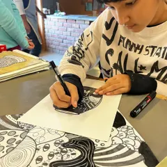 A close-up of a student drawing complex, doodle-like patterns with a fine-tipped marker.