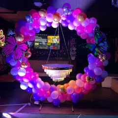 A whimsical butterfly-themed birthday decoration, perfect for making someone feel special. This circular balloon arch is adorned with large butterfly cutouts and features a hanging chandelier-style cake stand at its center.