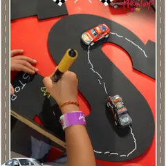A child carefully draws a path on a custom 'S' shaped racetrack for their toy cars. This activity combines creativity with the thrill of racing.