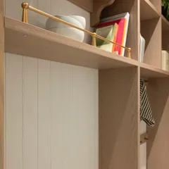 The brass railing on this open shelf is a small but elegant detail. It keeps cookbooks and decor items secure while adding a touch of warmth and sophistication to the wooden shelving.