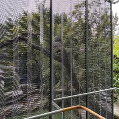 A view through the perforated metal screen we designed for a commercial building in Bangalore. The folded, layered skin acts as a veil, reducing glare and creating a dynamic play of light and shadow while offering a modern counterpoint to the surrounding greenery.