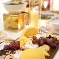 A beautifully lit close-up of a rustic cheese board. This platter features generous portions of various cheeses, including a soft Brie, paired with grapes, nuts, and crackers, set against a warm, candlelit backdrop.