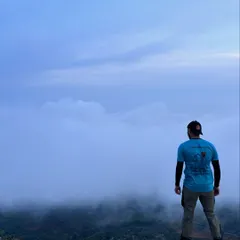 An instructor stands at the edge of a cliff, looking into a sea of clouds. We lead the way, finding the most inspiring spots for your team to explore.