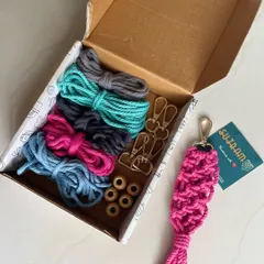 Here is a peek inside the box! You get five bundles of soft 3mm cotton cord, five golden hooks, and wooden beads, plus a finished pink keychain to show you what is possible. It is a perfect sustainable DIY gift idea.
