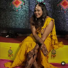 A happy bride posing for a photo during her mehandi ceremony, showcasing the full hand and leg designs I created for her.
