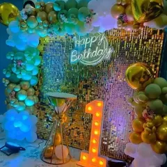 A first birthday party with a gold shimmer wall, a 'Happy Birthday' neon sign, and a '1' marquee light.