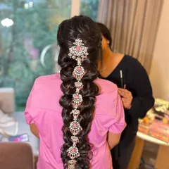 The finished hairstyle for the Varapooja. This is a modern take on a traditional braid, using stunning pink and white stone-studded accessories instead of fresh flowers.