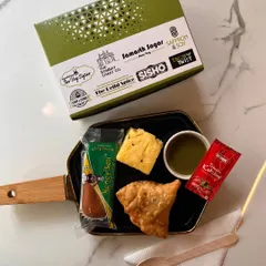 A duplicate of our classic snack box, this image again shows the popular combination of a samosa, dhokla, and a sweet treat. The consistent quality and presentation are key to our service.