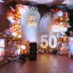 Celebrating a 50th birthday in style! This elegant setup features a 'Let's Party' neon sign, a sophisticated rose gold and white balloon arch, and large light-up marquee numbers. I also added personalized photo cubes to display cherished memories, making the celebration deeply personal.