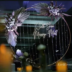 A dreamy, softly lit view of our boho-chic proposal ring. The combination of dried palm leaves, white flowers, and cascading fairy lights creates a whimsical and romantic setting.