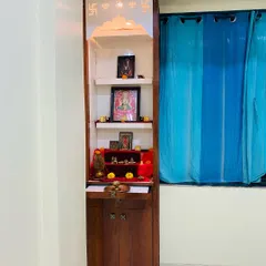 A compact pooja unit designed for a bedroom. This slim, elegant cabinet features storage and a beautifully lit space for daily prayers.