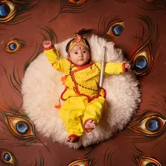 A beautiful top-down shot of a baby dressed as Krishna, lying on a bed of peacock feathers.