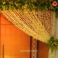 The fragrant and delicate beauty of tuberose (rajnigandha) makes for a stunning entrance. We crafted this asymmetrical curtain from strings of white tuberose, elegantly draped across the doorway and complemented by lush greenery.
