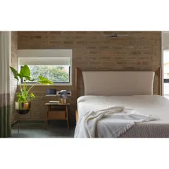 A bedroom in the renovated Hyderabad residence. The exposed brick wall adds warmth and texture, while the simple window frames a view of the surrounding greenery, creating a calm and restful atmosphere.
