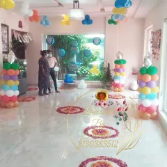 The indoor setup for the welcome baby boy party. The room is filled with rainbow-colored balloon pillars and flower rangoli on the floor, creating a bright and cheerful atmosphere.
