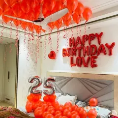 A vibrant red-themed 25th birthday bedroom decoration, with red balloons on the ceiling, 'Happy Birthday Love' foil letters, and number balloons.