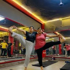 Two participants enjoying a partner standing split pose. My classes are a space for fun, encouragement, and shared achievement.