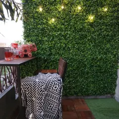 This image shows a close-up of an artificial green wall illuminated by string lights. Next to it, we used interlocking wood deck tiles to create a durable and stylish floor for the bar area, demonstrating how different textures can define a space.