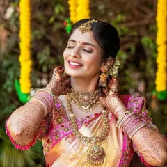 A picture of pure bridal joy. Her natural makeup look, with soft eyes and a bright smile, is paired with a traditional updo and gold jewelry for her wedding day.