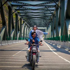 A couple enjoys a scenic motorcycle ride across a bridge, capturing a sense of freedom and adventure in their pre-wedding shoot.