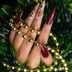 A festive Christmas look featuring sculpted stiletto extensions. This set combines deep red glitter nails with nude accent nails, which are detailed with hand-painted reindeer art for a touch of holiday magic.