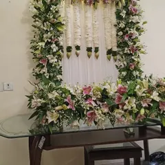 A close-up of the Ganpati decoration made with pink and white lilies, with hanging tuberose (rajnigandha) garlands against a white curtain.