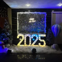A dramatic New Year's Eve decoration for 2025. This setup features large, illuminated marquee numbers, a shimmering sequin wall, and atmospheric blue lighting to create a cool, celebratory vibe for a countdown party.