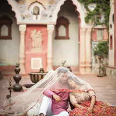 A moment of serene togetherness, draped under a delicate veil. This composition uses the heritage courtyard and traditional attire to tell a story of classic Indian romance.