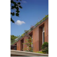A view of the U-L-I Residence's upper level, where a rooftop garden and planters are integrated into the architecture. The rust-colored facade panels contrast beautifully with the lush greenery, creating a warm, natural aesthetic.