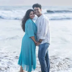 A happy couple portrait taken right at the water's edge. They are holding hands and smiling at the camera, capturing a perfect moment of joy during their beach maternity session.