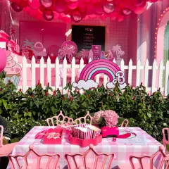 A view of the Barbie-themed party setup, complete with a rainbow, pink picket fence, and custom table settings. Every detail was designed to create a magical atmosphere.