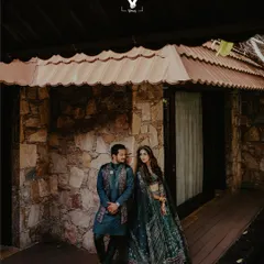 A duplicate of image 21, this portrait shows a couple sharing a look while standing on the wooden porch of a rustic stone cottage, blending elegant attire with a natural setting.