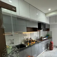 A modular kitchen at a housewarming in Ramamurthy Nagar. The design features glossy grey cabinets, a marble-patterned backsplash, and under-cabinet lighting for a modern and functional workspace.