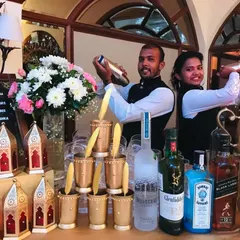 Flair and function combined. My bartenders showcase their skills with cocktail shakers at a beautifully arranged Sufi bar, complete with premium spirits, fresh flowers, and stacks of ornate brass glasses.