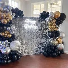 A silver and black sequin wall provides a dazzling photo backdrop. The setup is framed by an organic balloon garland in matching colors, perfect for a stylish birthday party or event.