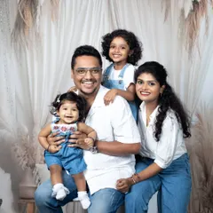A happy family of four posing together in the studio, dressed in matching white and denim outfits for a clean, classic look.