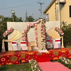 A beautiful outdoor Nikah partition setup for a daytime ceremony. The stage is decorated with a floral arch of pink and white roses and a central partition of hanging white flowers.