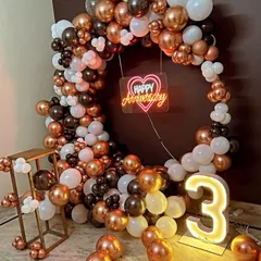 Celebrate your years together with a modern and stylish anniversary decoration. This circular balloon arch in a chic rose gold, white, and black theme, complete with a 'Happy Anniversary' neon sign and a light-up number, makes for a perfect photo backdrop.