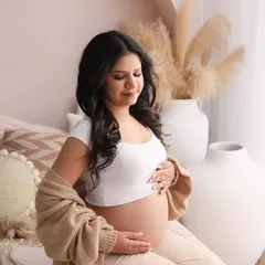 This is a portrait of peaceful connection, a mother taking a quiet moment to feel the life growing within. The soft knit cardigan and neutral tones add to the cozy, intimate feeling.
