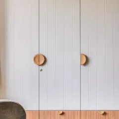 This master wardrobe continues the home's transitional design language, featuring sleek white grooved shutters with natural wood accents and custom circular wooden handles.
