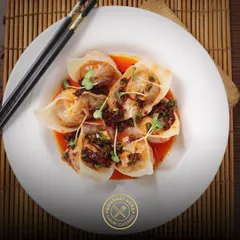 A plate of delicate wontons served in a savory chili oil broth, garnished with fresh microgreens. This dish perfectly balances spice, flavor, and texture.