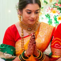 A candid moment of a Maharashtrian bride during her ceremony. The makeup is kept soft and radiant with golden hues to match her jewelry, and the hair is styled in a traditional updo with fresh flowers.
