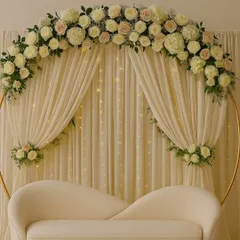 A beautiful and sophisticated stage design with a white and pastel floral arch. The backdrop of cream drapes with fairy lights and a modern white sofa creates a dreamy and elegant setting.