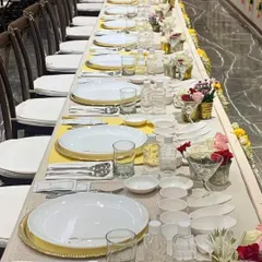 A long dining table meticulously set for a traditional feast. The combination of white and yellow linens, along with fresh flowers, creates a bright and welcoming atmosphere for guests.