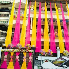 A full view of a multi-story house decorated with long, flowing drapes in pink and yellow. This kind of decoration instantly signals a celebration in the neighborhood.