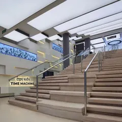 The grand staircase inside the museum, referred to as the 'Time Machine'. The design uses clean lines, modern materials like glass and steel, and dramatic back-lit panels to create a futuristic feel.