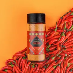 This image for a peri-peri seasoning uses a bed of vibrant red chillies and a bold orange background to make the product pop. This is a great example of a clean, product-focused shot that is ideal for e-commerce websites and online advertising.