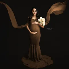 A fine-art maternity portrait featuring a flowing brown gown against a dark studio backdrop. The use of fabric in motion adds a dramatic and elegant effect to this solo pregnancy photo.