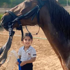 A smiling child helps wash a horse, learning to be gentle and confident around these large animals.