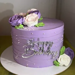 Simple, pretty, and classy, this purple whipped cream cake is adorned with hand-piped florals in shades of purple and white. The clean lines and delicate details make it a truly elegant choice.